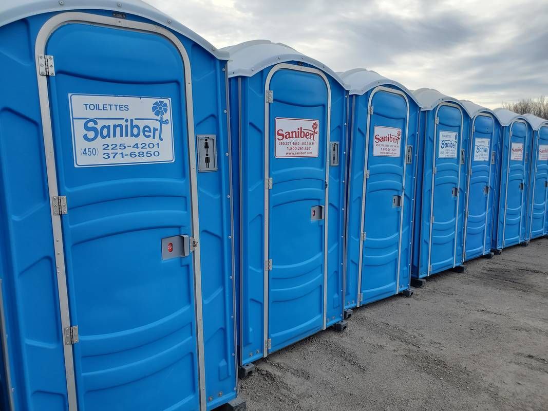 Rangée de toilettes portables bleues dans un cadre extérieur, avec signalisation sur les portes.