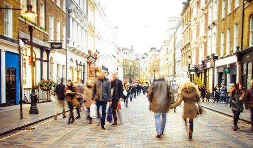 Des passants dans une rue de Londres, des boutiques bordant les rues. Ciel couvert.