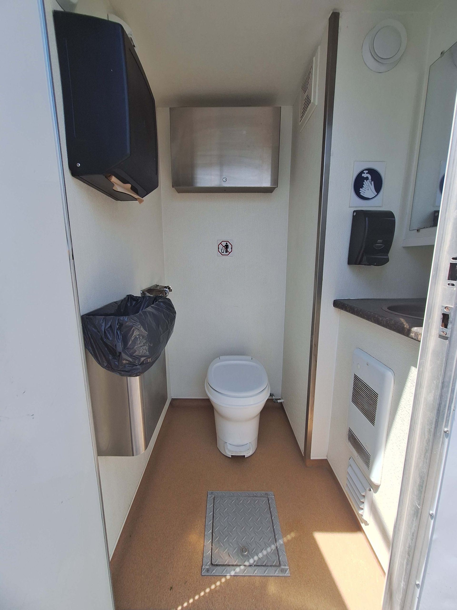 Intérieur de toilettes portables avec WC, lavabo et poubelle. Murs blancs, sol marron.