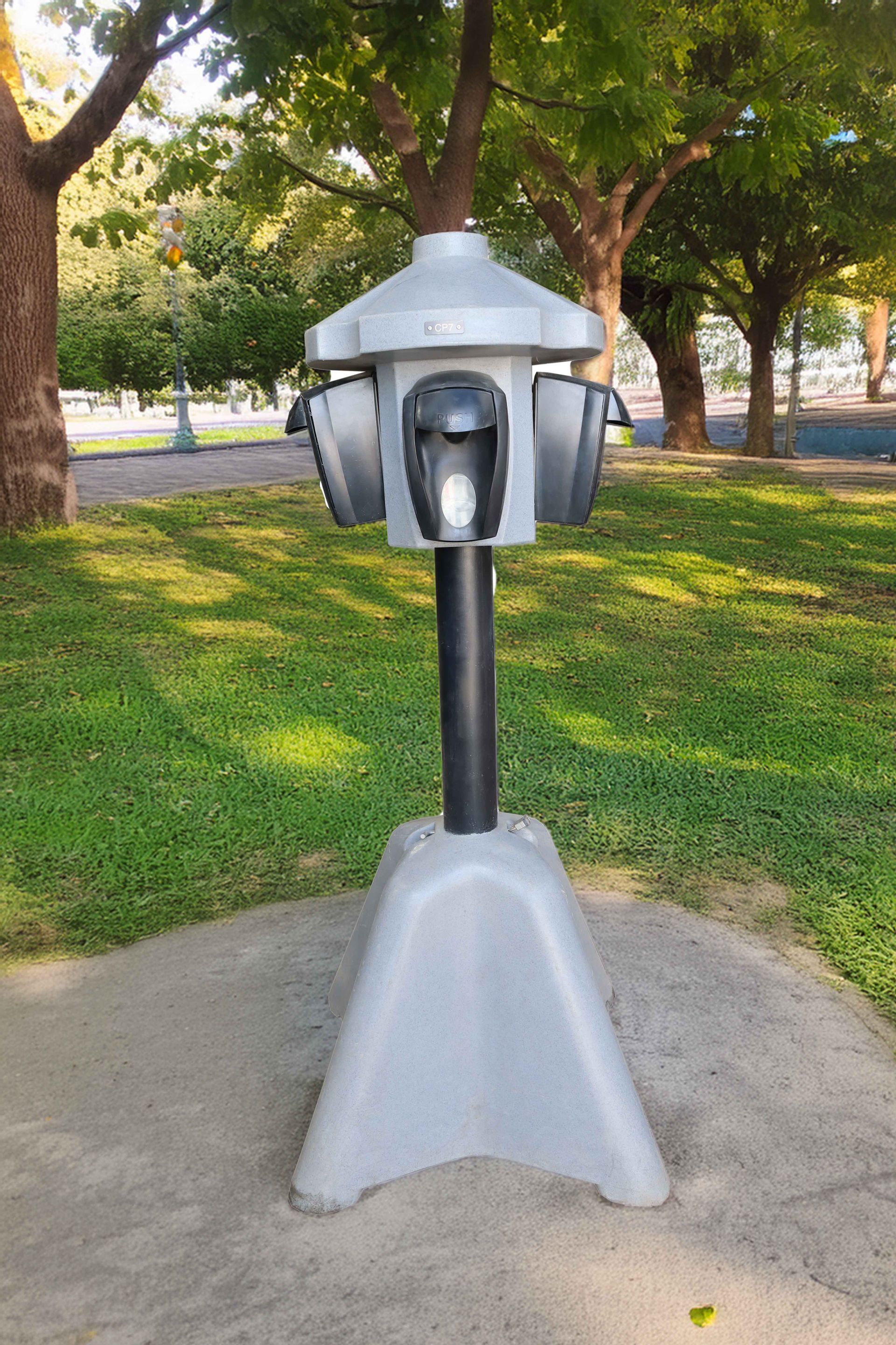 Distributeur de sacs à déjections canines dans un parc, gris avec poteau noir.