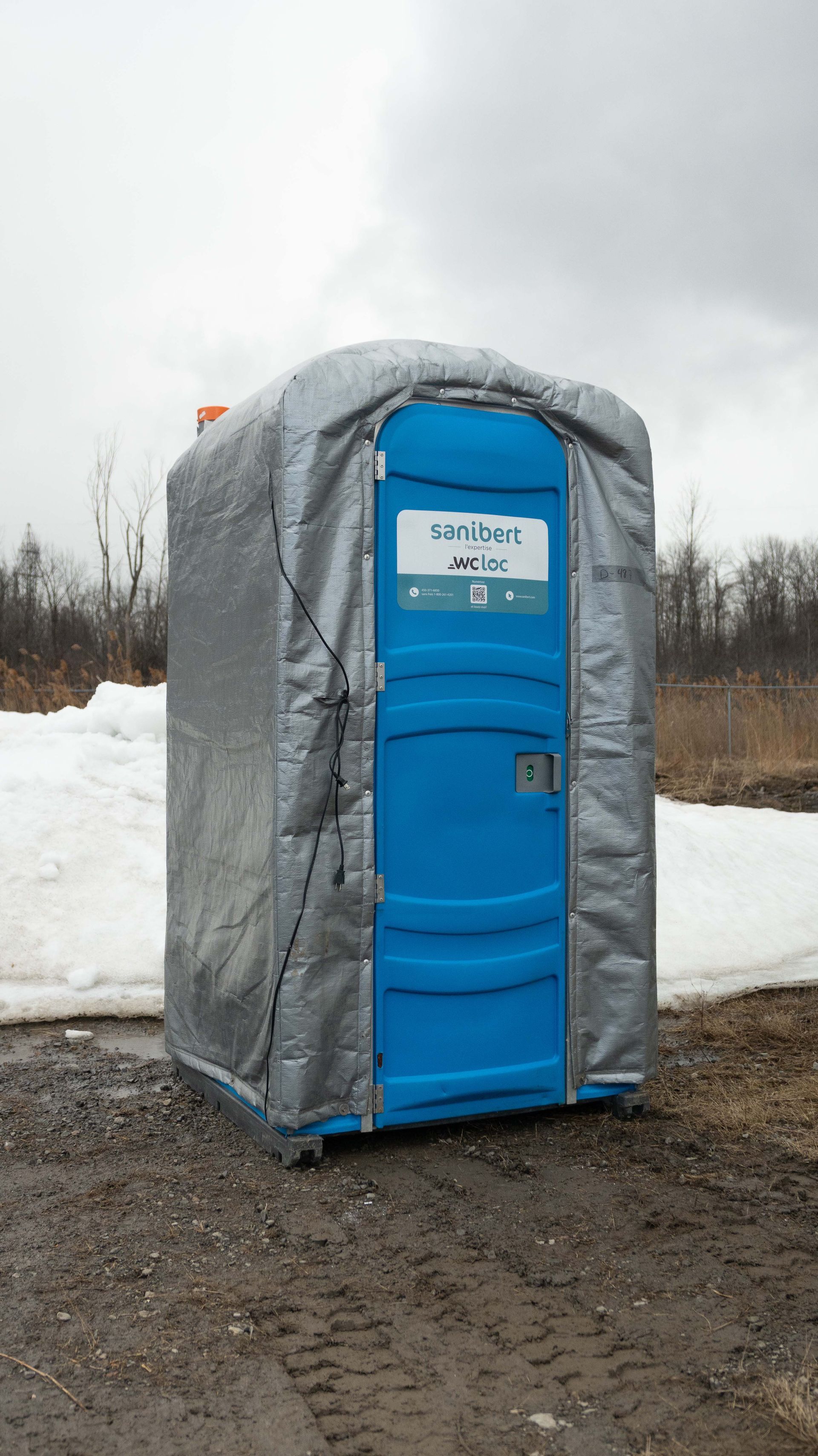 Toilettes portatives bleues recouvertes d'une isolation argentée dans un décor extérieur enneigé.