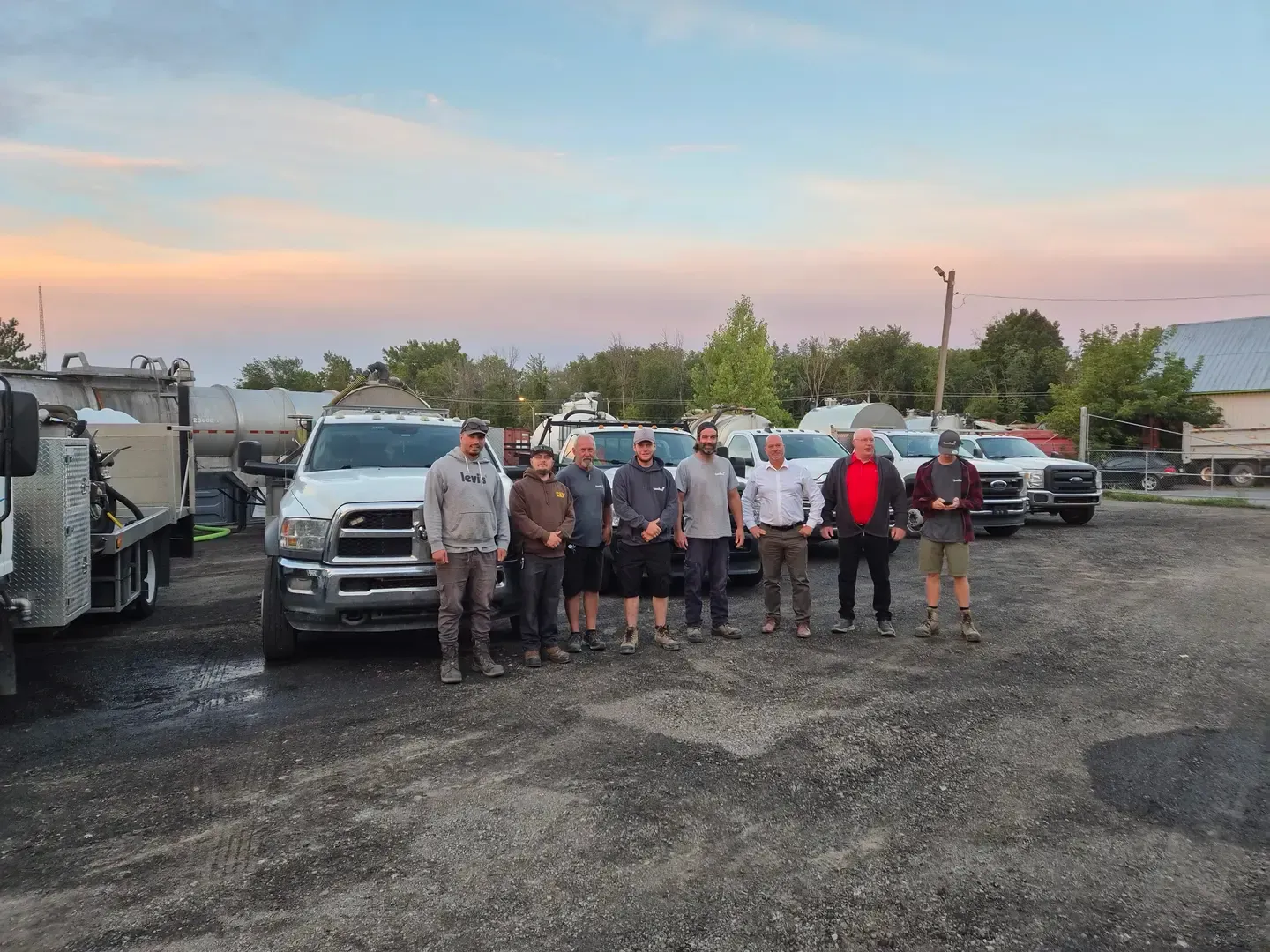 Groupe d'hommes debout devant des camions au crépuscule.