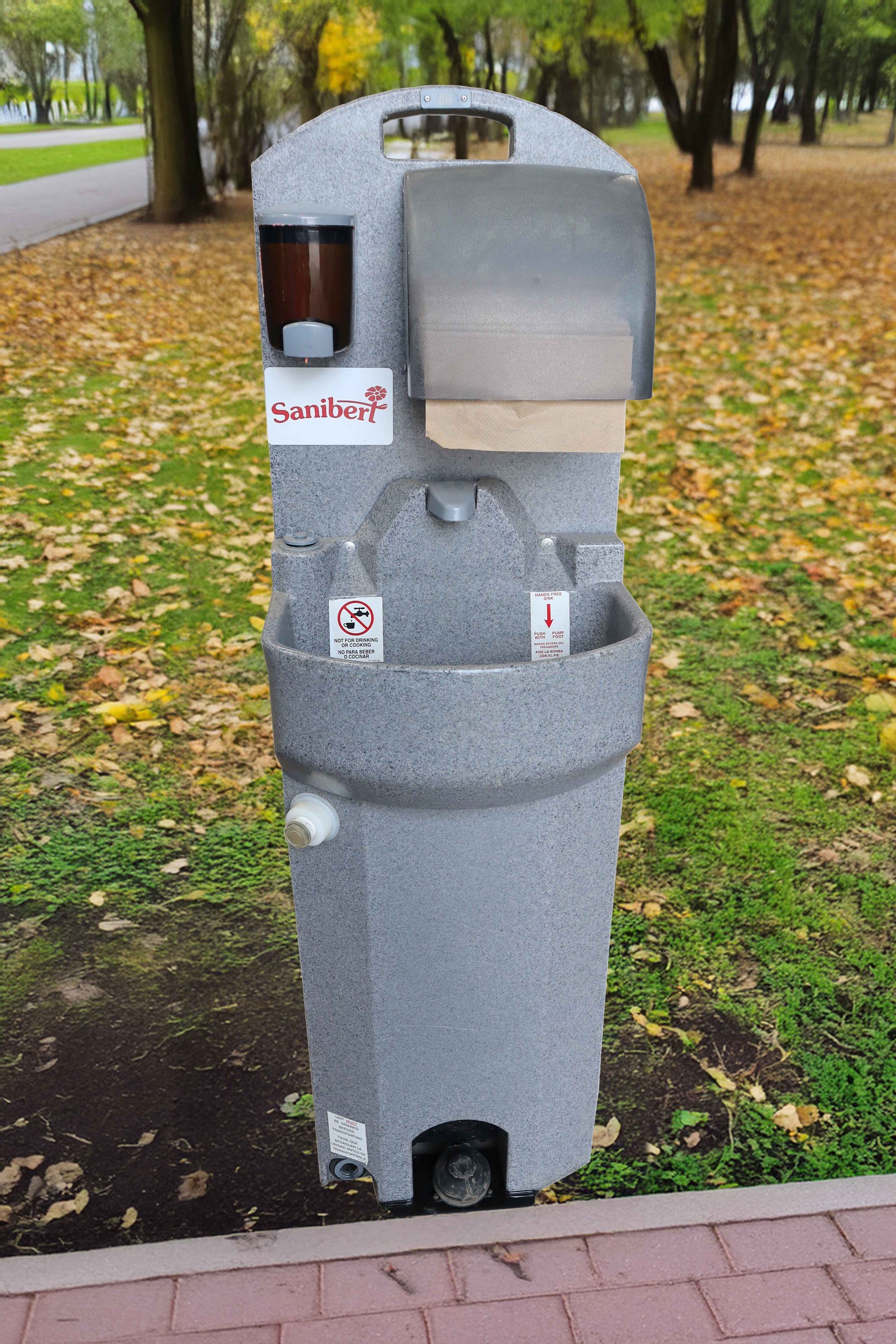 Station de lavage des mains extérieure avec savon, serviettes en papier et bouteilles, dans un parc.