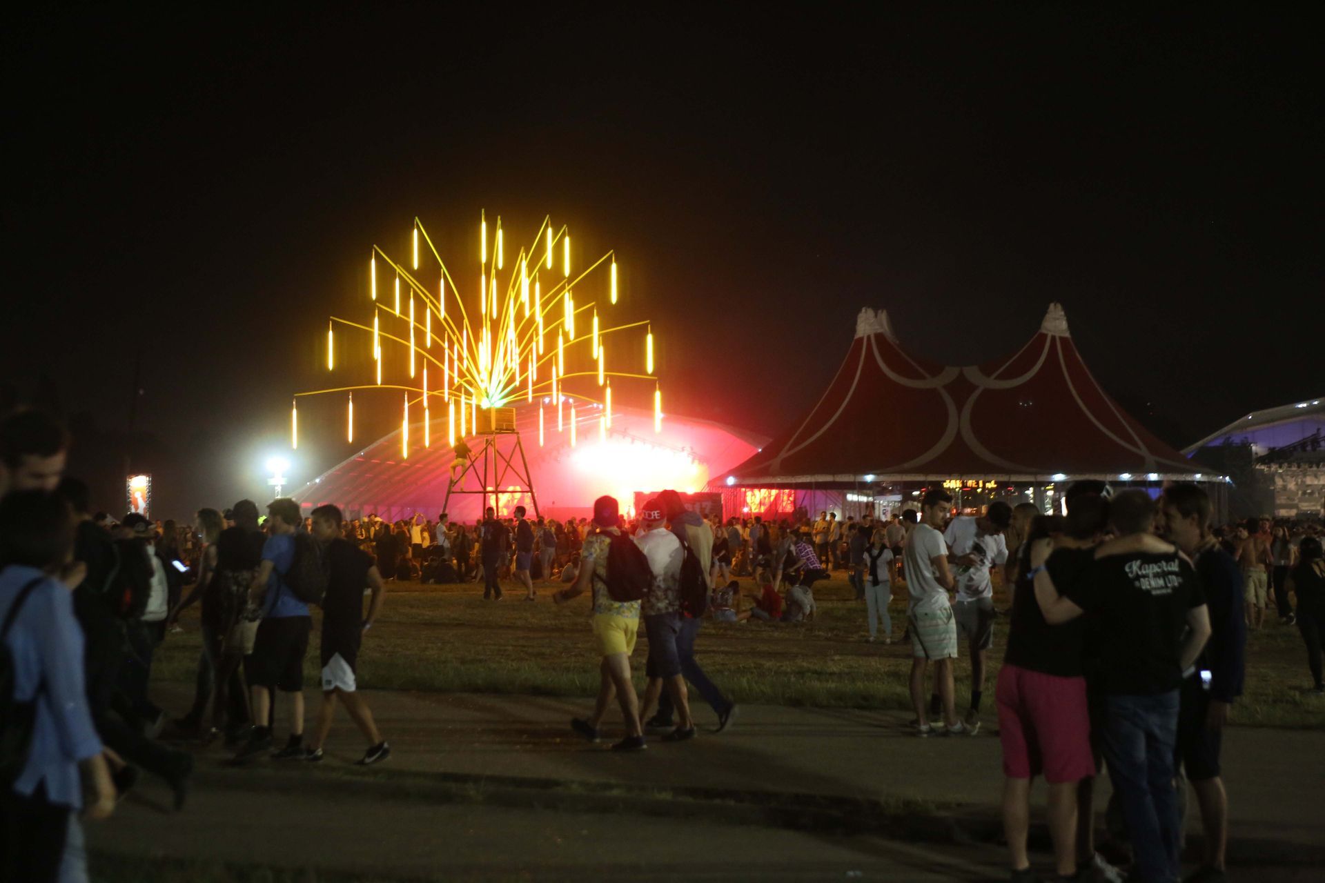 Festival nocturne en plein air avec grande roue éclairée, scène, foule.