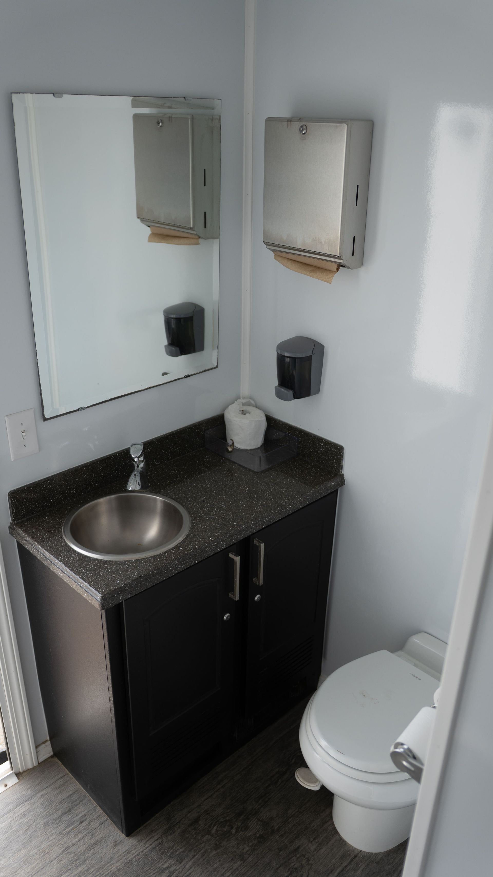 Remorque de toilettes portables blanches avec logo rouge, posée sur du gravier.