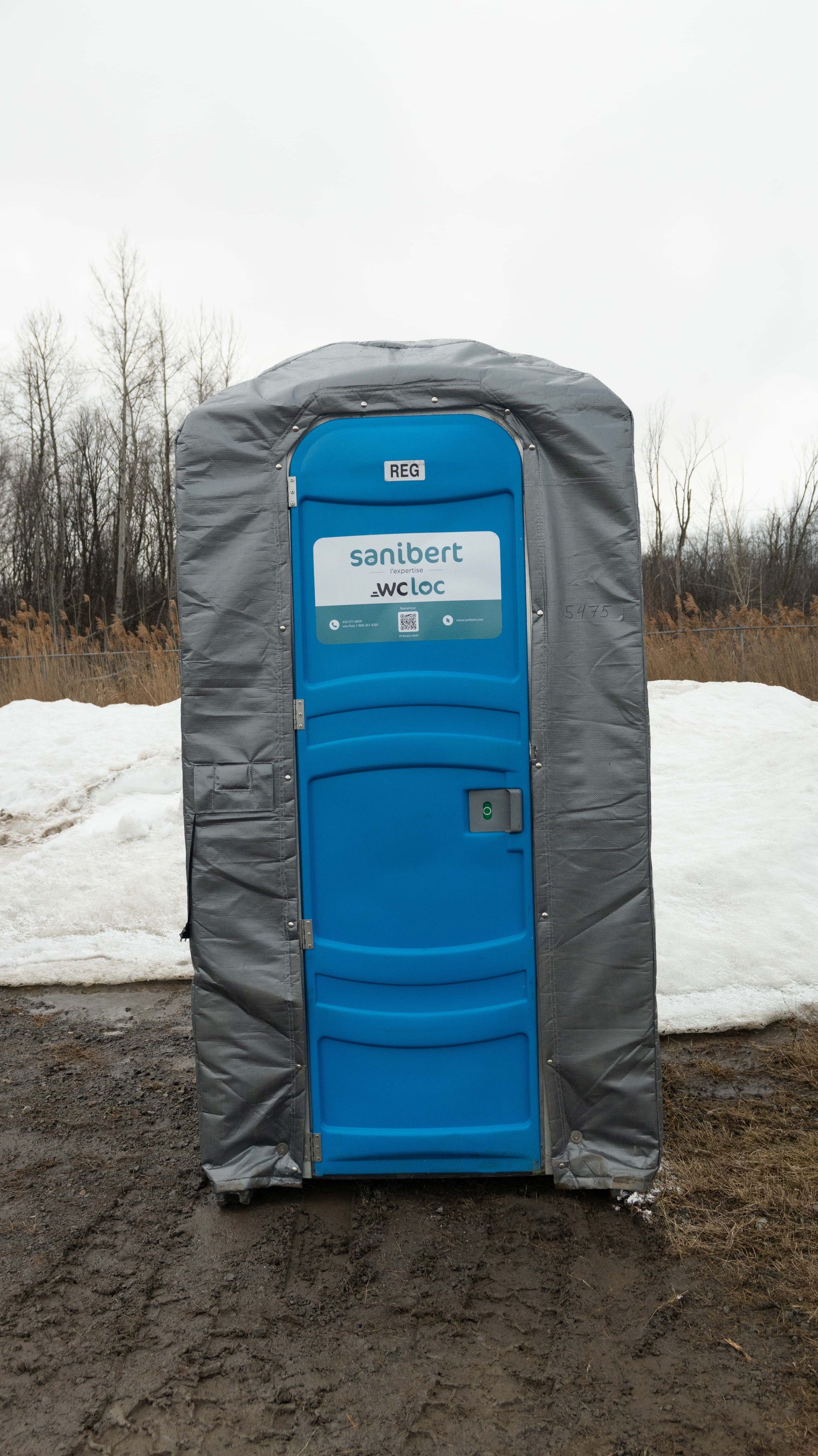 Toilettes portables grises sur gravier, près des voies ferrées.