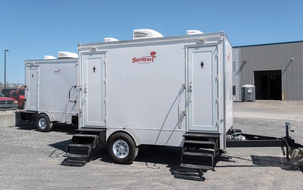 Deux toilettes portables blanches sur roues avec marches, sous un ciel bleu.