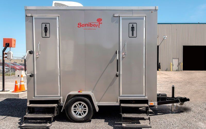 Toilettes mobiles mobiles avec entrées séparées pour hommes et femmes. En métal argenté, installées à l'extérieur.