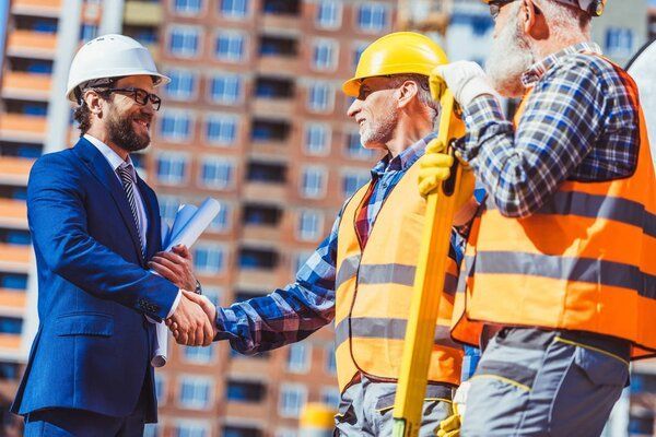 Un homme en costume serrant la main d'ouvriers du bâtiment sur un chantier.