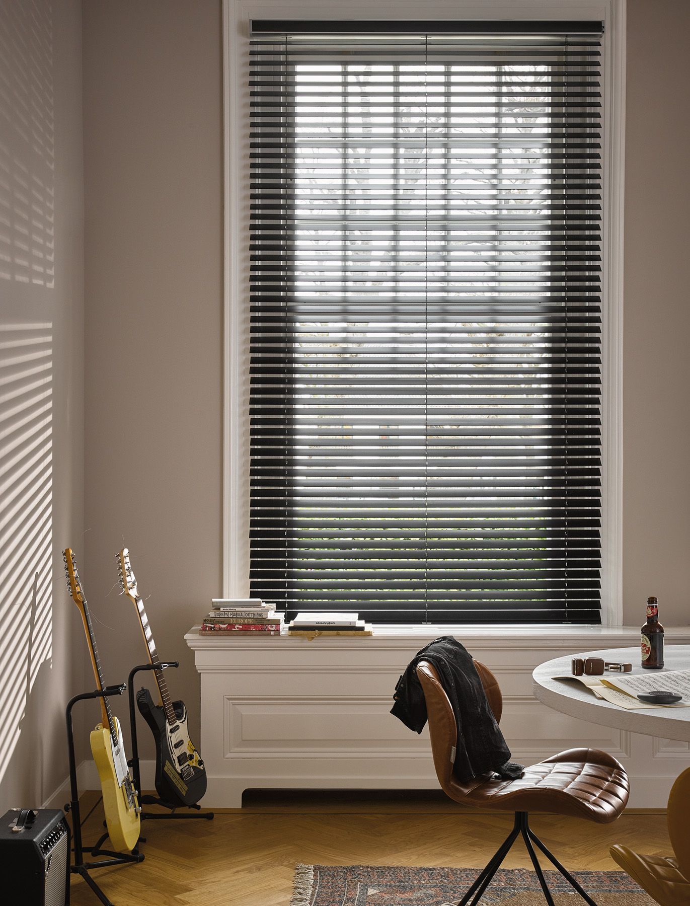 A room with a table , chair , guitars and blinds on the window.