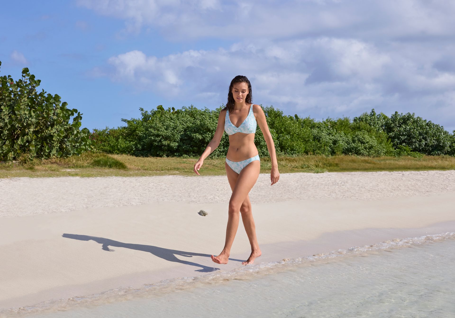 Une femme en bikini marche sur une plage.
