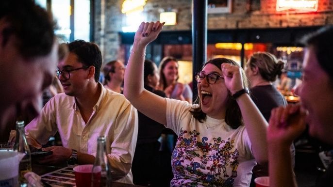 Group of ten women posing together at a bar; most wear black dresses, smiling at the camera.
