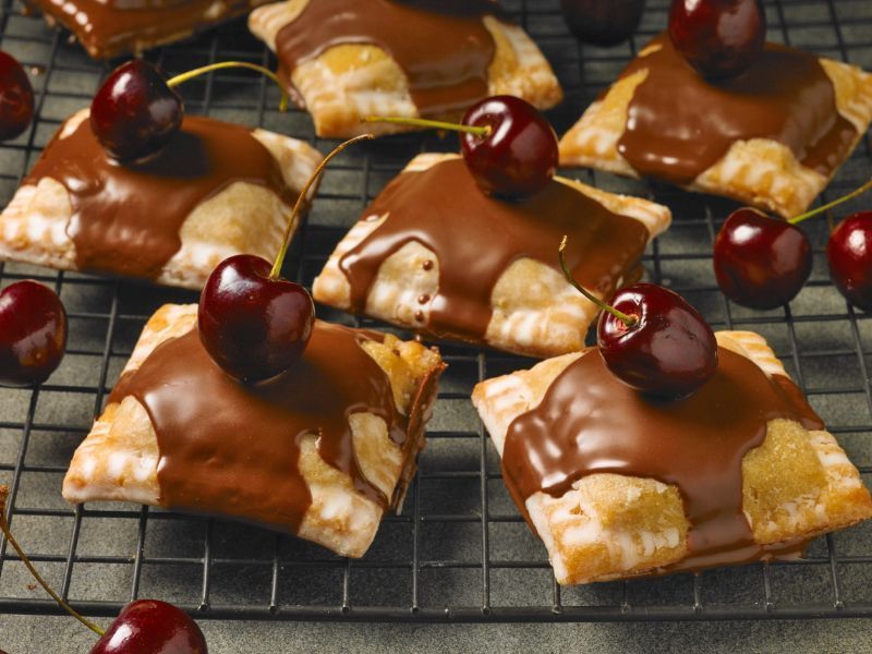 cherry pies topped with chocolate drizzle on a wire baking rack
