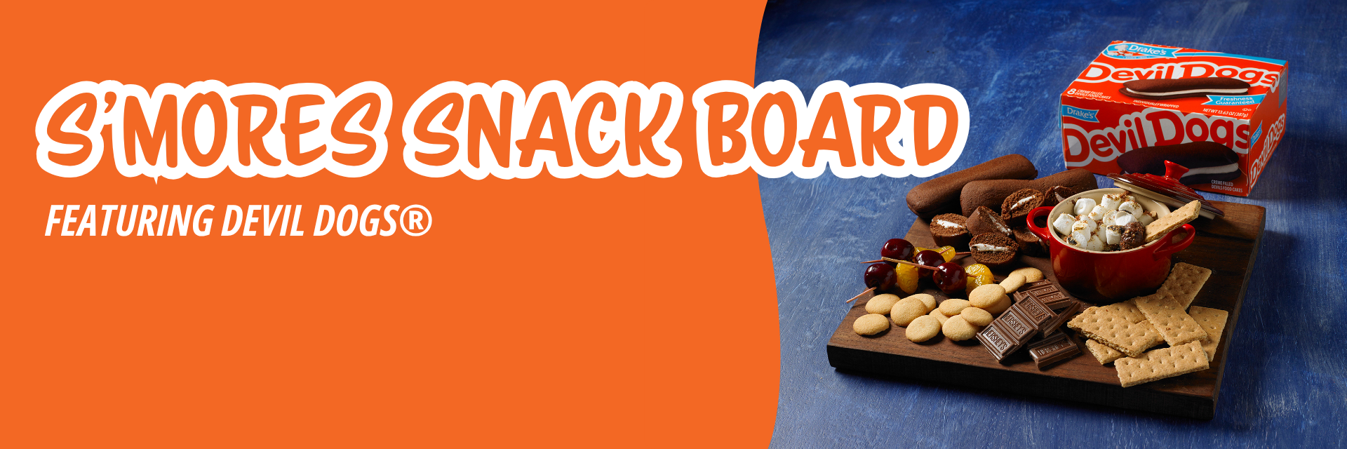 Orange banner promoting a wooden board with Devil Dogs, s'mores dip, graham crackers, cookies, cherries, and chocolate against a blue background.