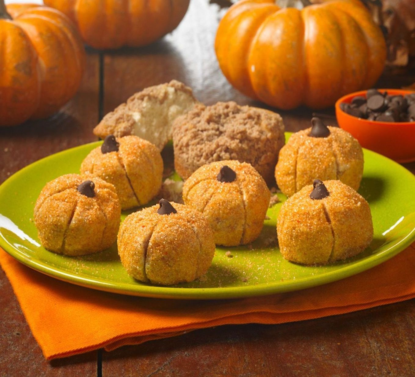 A green plate topped with cookies in the shape of pumpkins