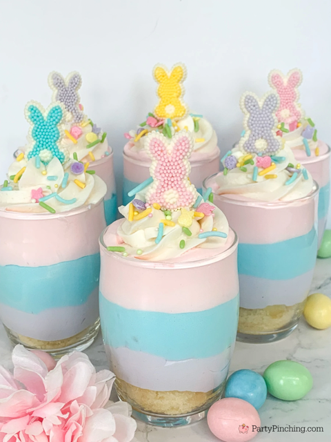 Easter-themed dessert cups layered with pastel colors, topped with whipped cream, colorful sprinkles…