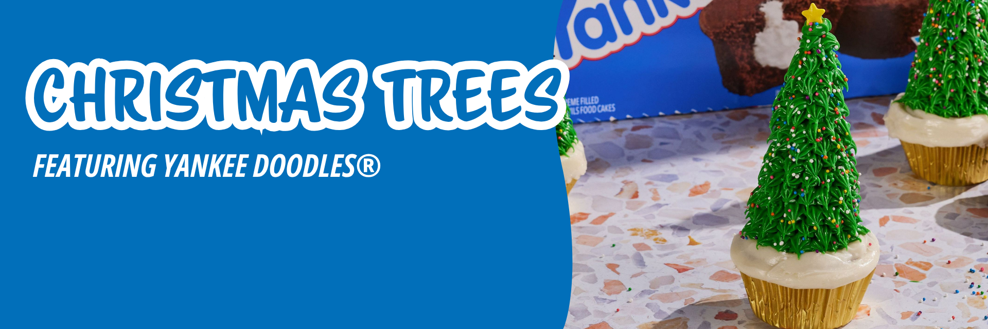 Blue banner promoting three cupcakes decorated to look like Christmas trees with green piped icing and stars on a speckled surface.