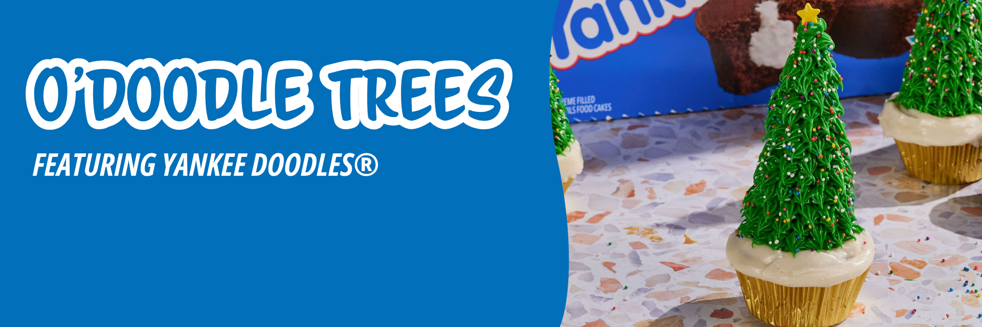 Blue banner promoting three cupcakes decorated to look like Christmas trees with green piped icing and stars on a speckled surface.