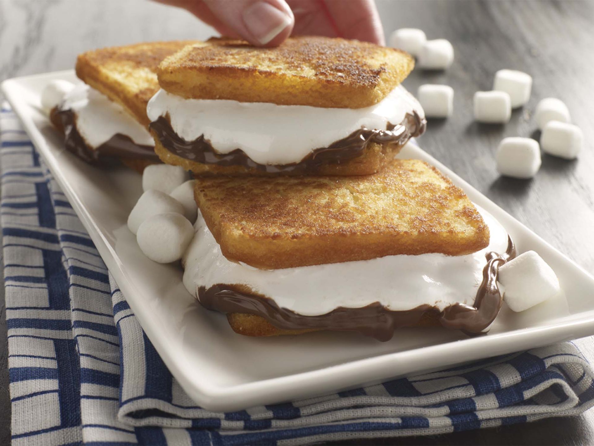 A white plate topped with s'mores sandwiches and marshmallows