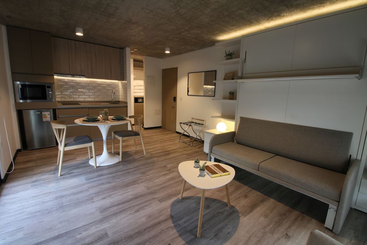 Moderno apartamento tipo estudio con cocina, comedor y sala de estar con sofá y mesa pequeña.