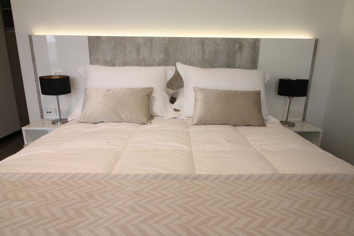 Una cama cuidadosamente hecha con almohadas beige, sábanas blancas y lámparas negras