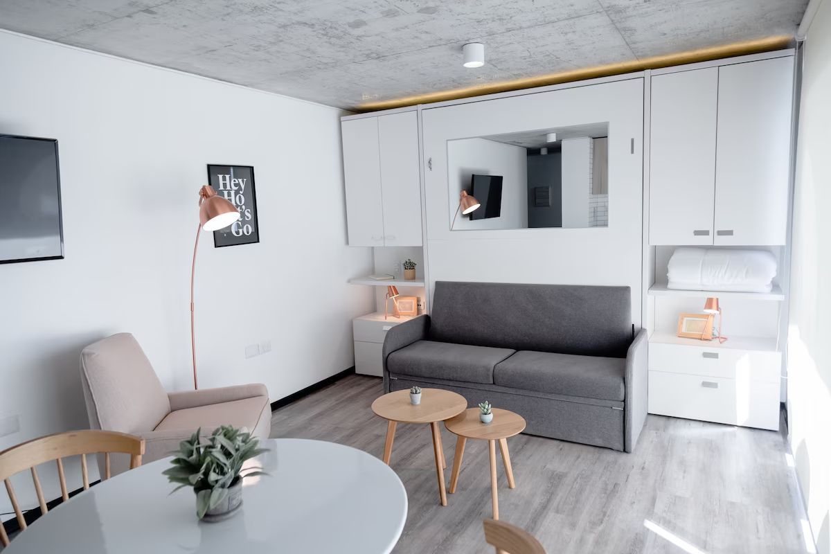 Sala de estar con sofá gris, paredes blancas, mesa redonda, suelos de madera y una estética moderna.