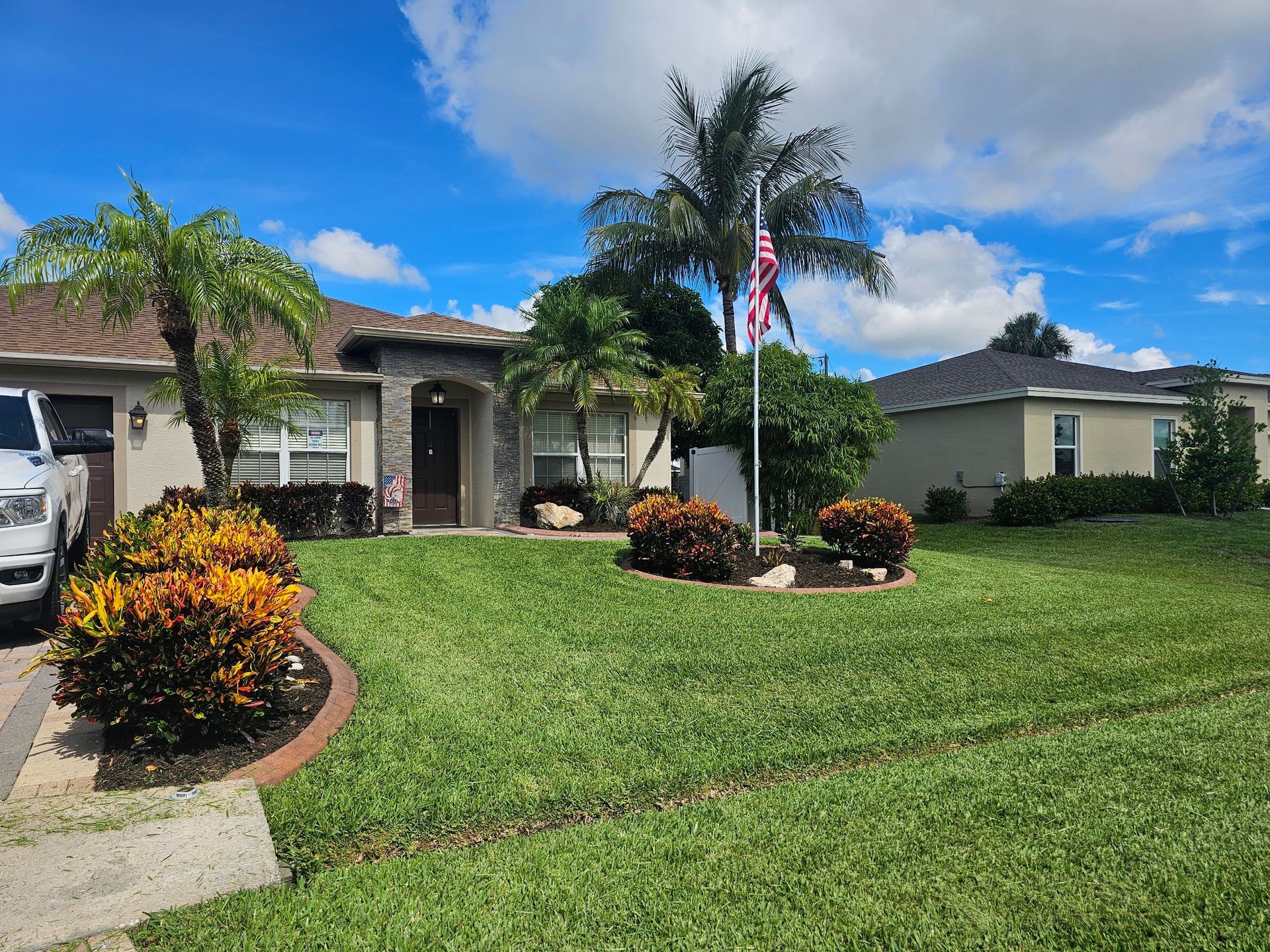 A white truck is parked in front of a house with a flag pole.