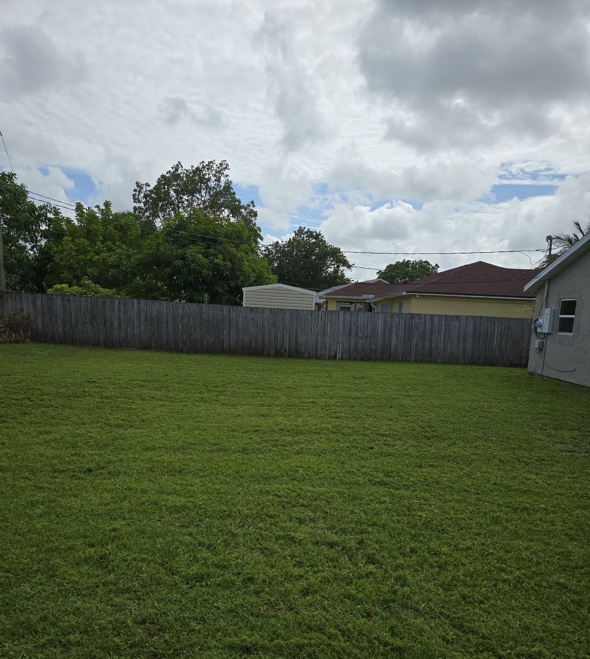 A backyard with a wooden fence and a house in the background