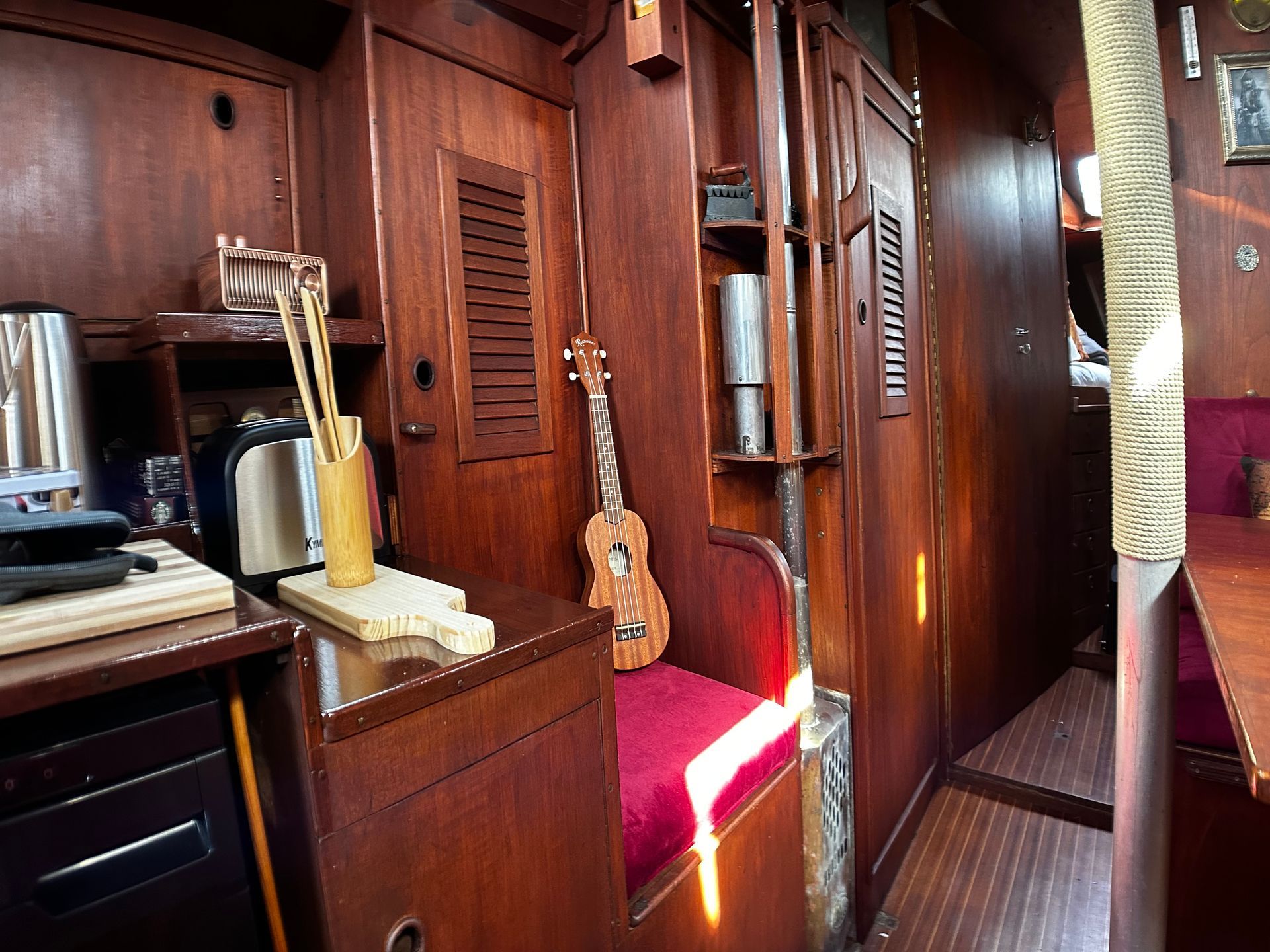 A guitar is sitting on a red cushion in a wooden room.