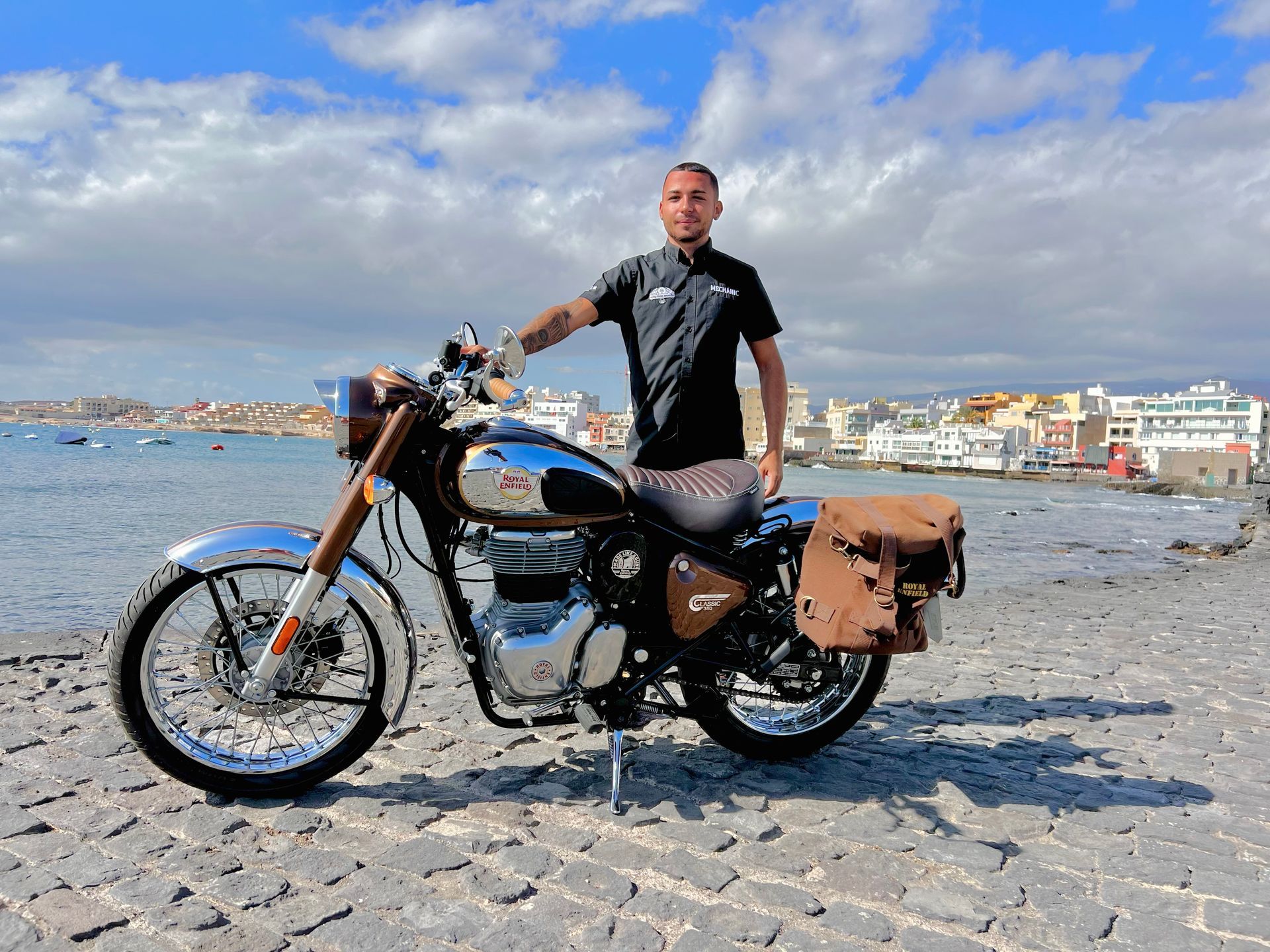 A man is standing next to a motorcycle on the beach.