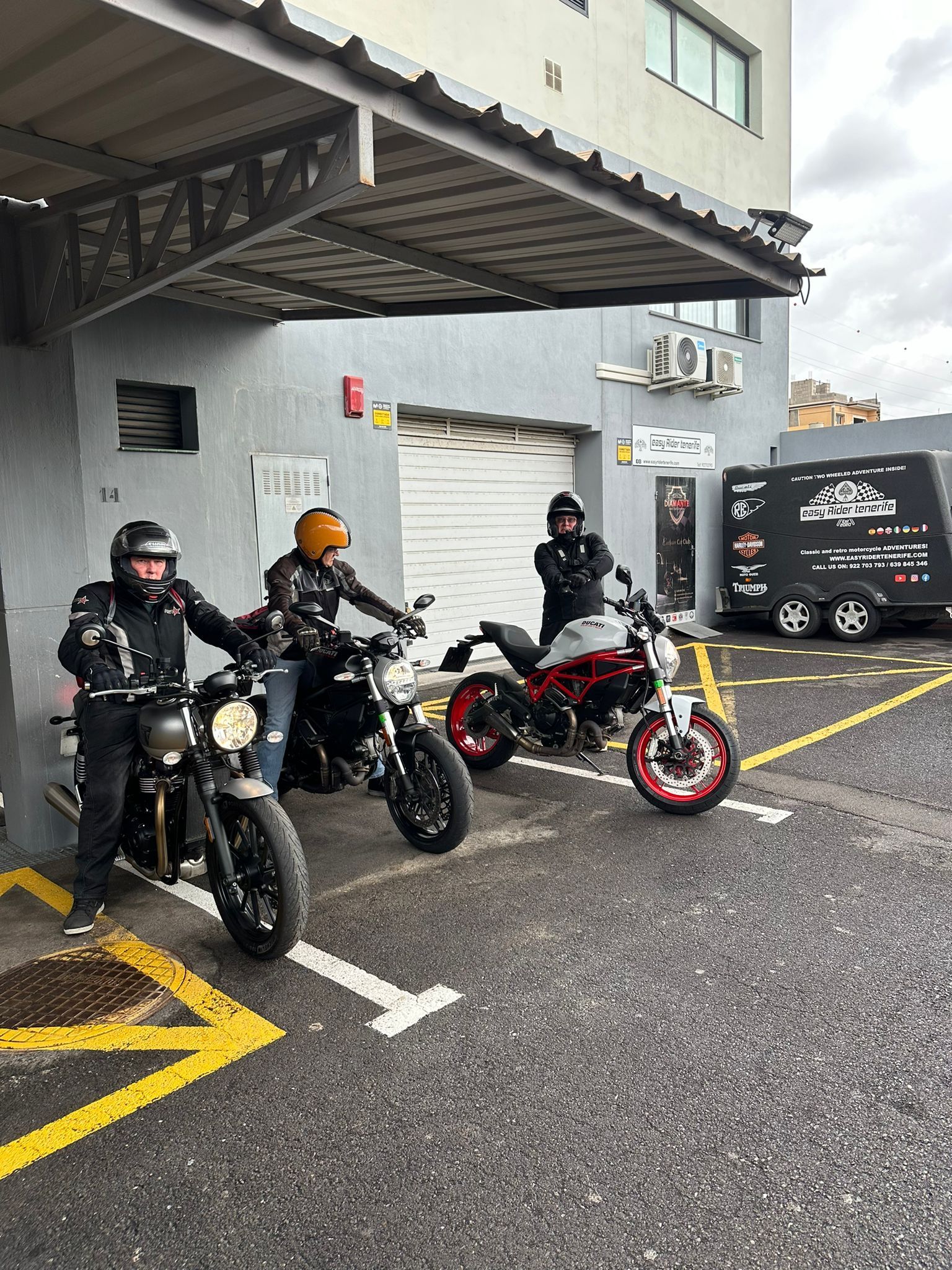 Three people are riding motorcycles in a parking lot.