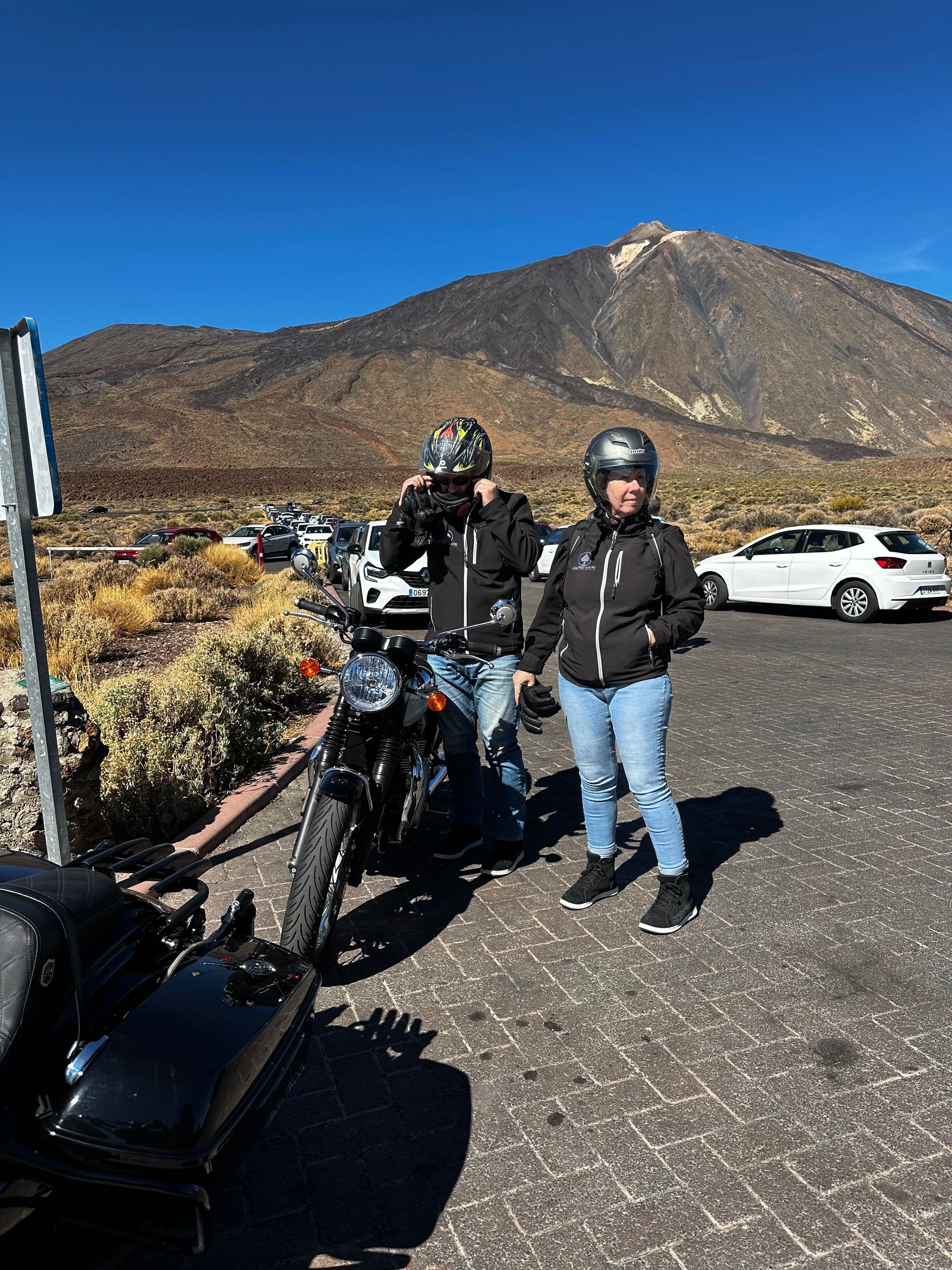 Two people are standing next to a motorcycle in a parking lot.