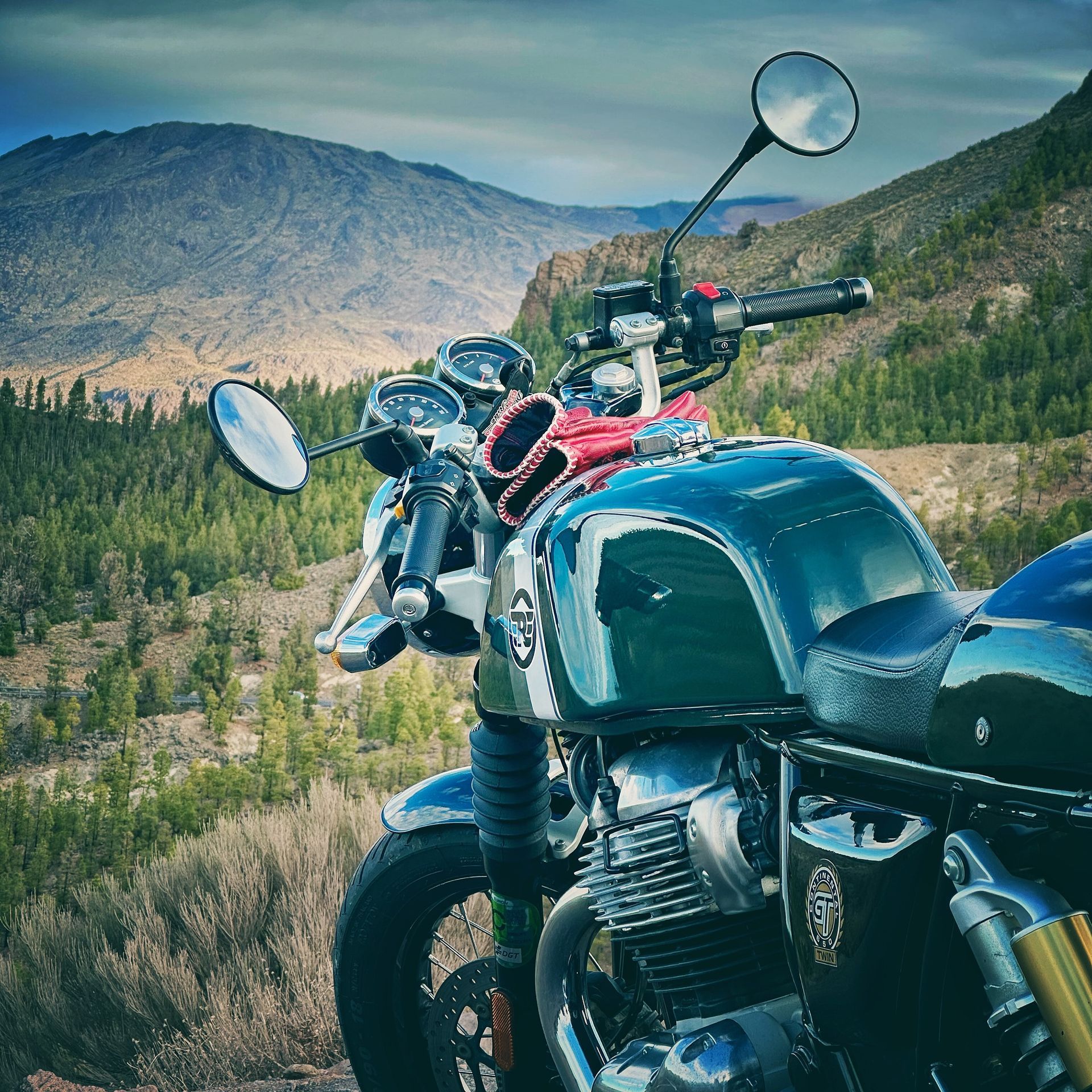 A motorcycle is parked on top of a hill with mountains in the background.