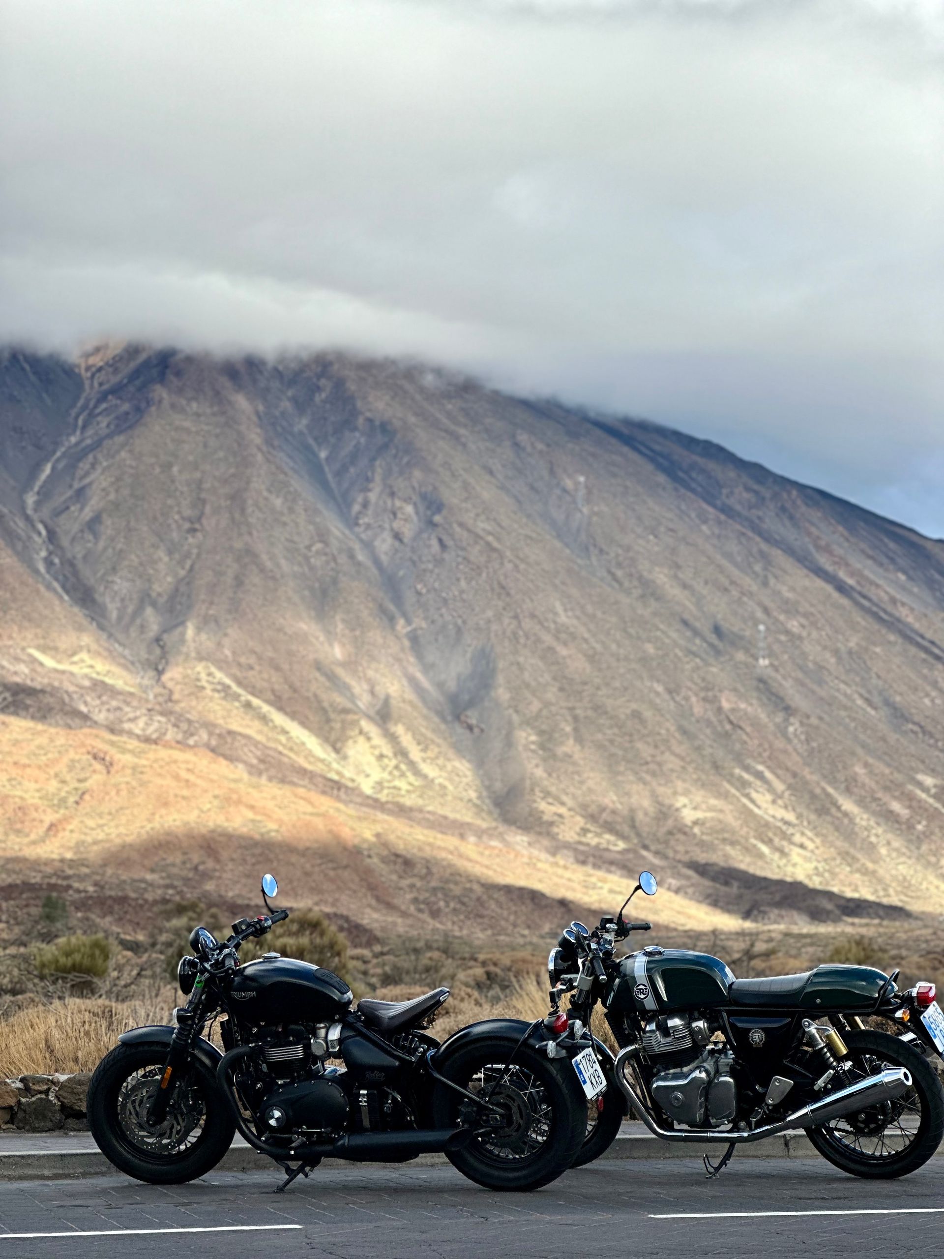 Two motorcycles are parked on the side of the road in front of a mountain.