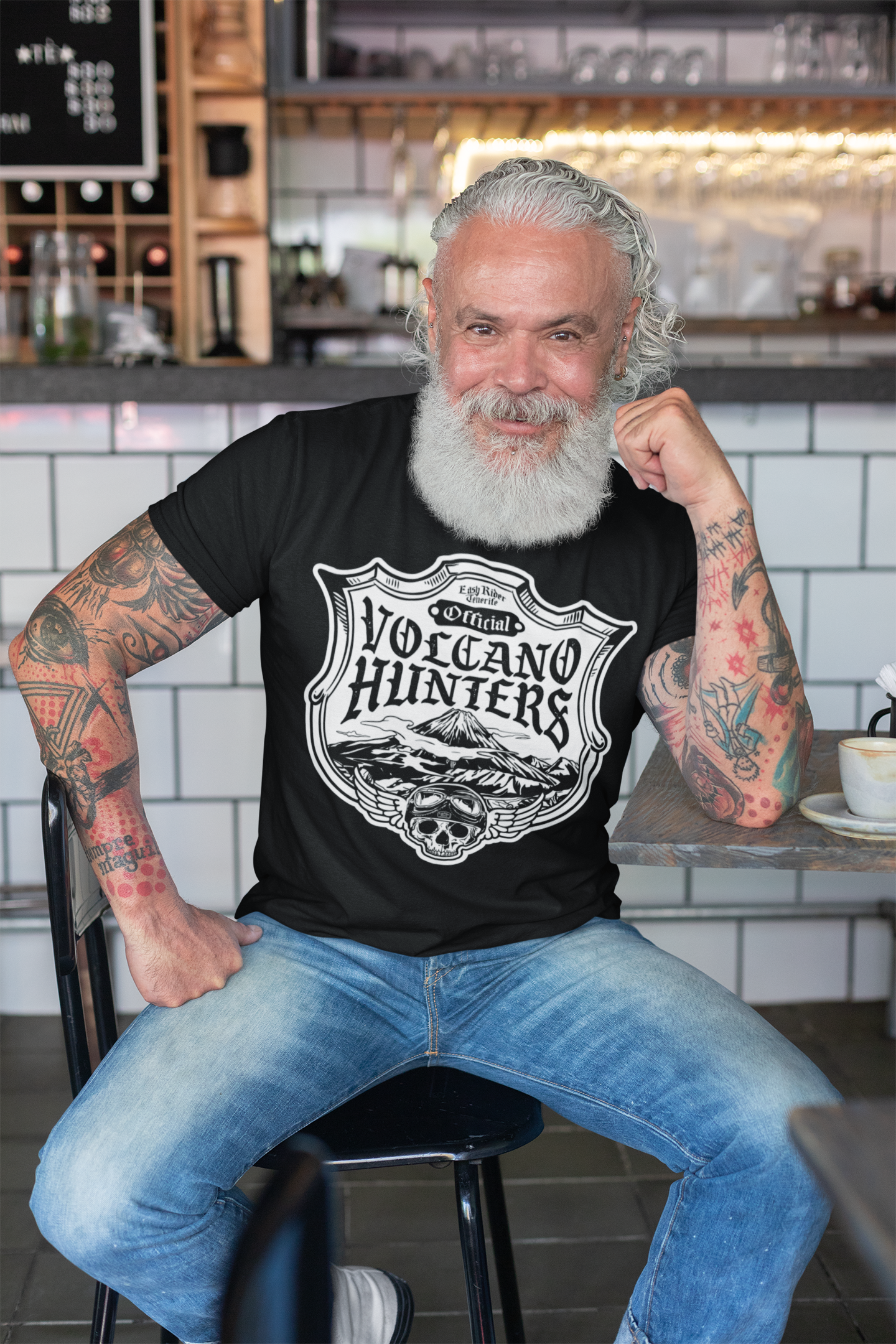 A man with a beard and tattoos is sitting at a table in a restaurant.