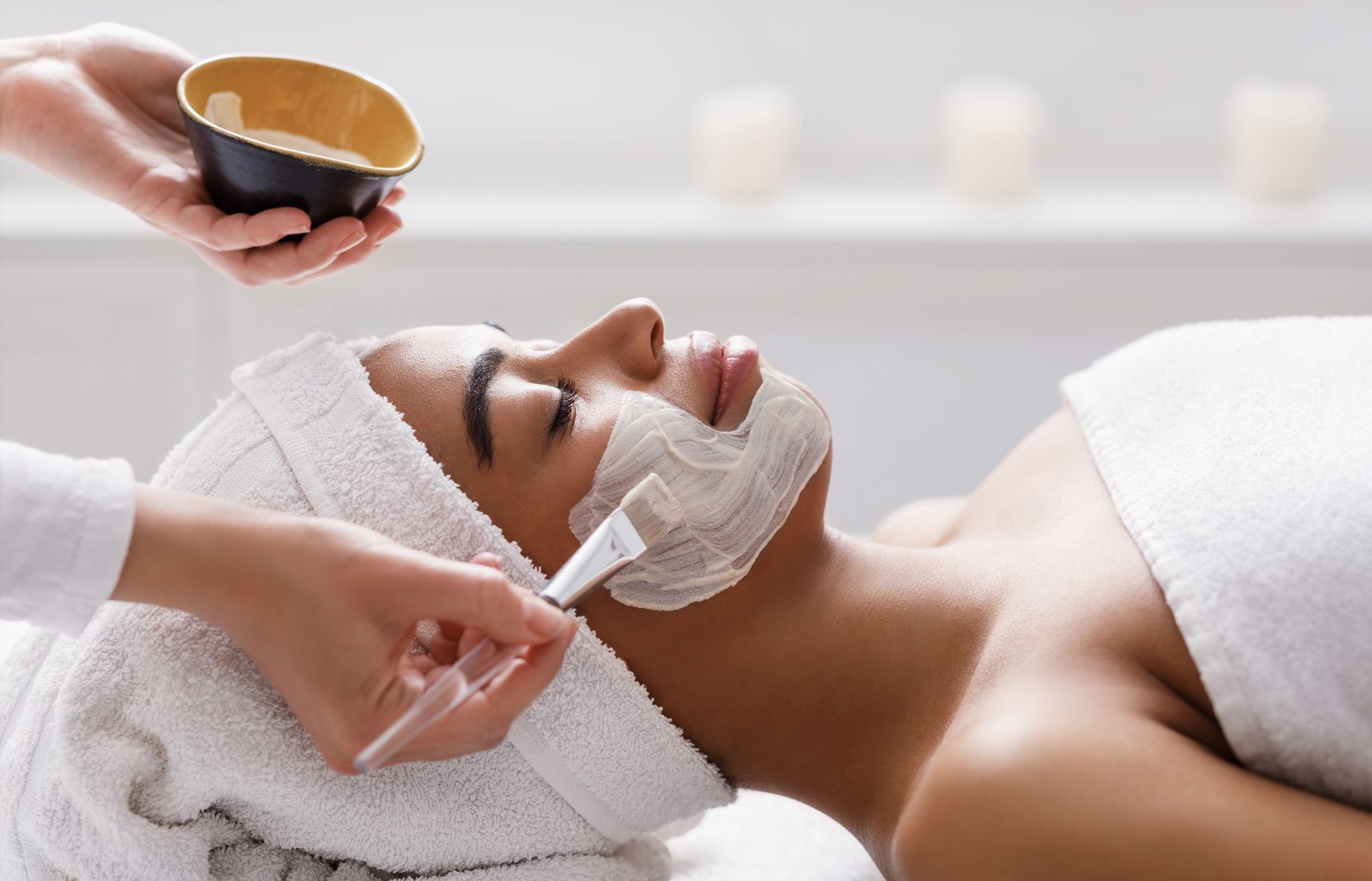 Person receiving facial mask at a spa. A bowl and brush are being used to apply the mask.