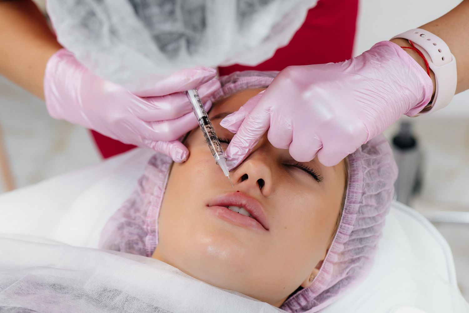 Cosmetic procedure on a woman's face with gloved hands using a syringe near her nose and eye area