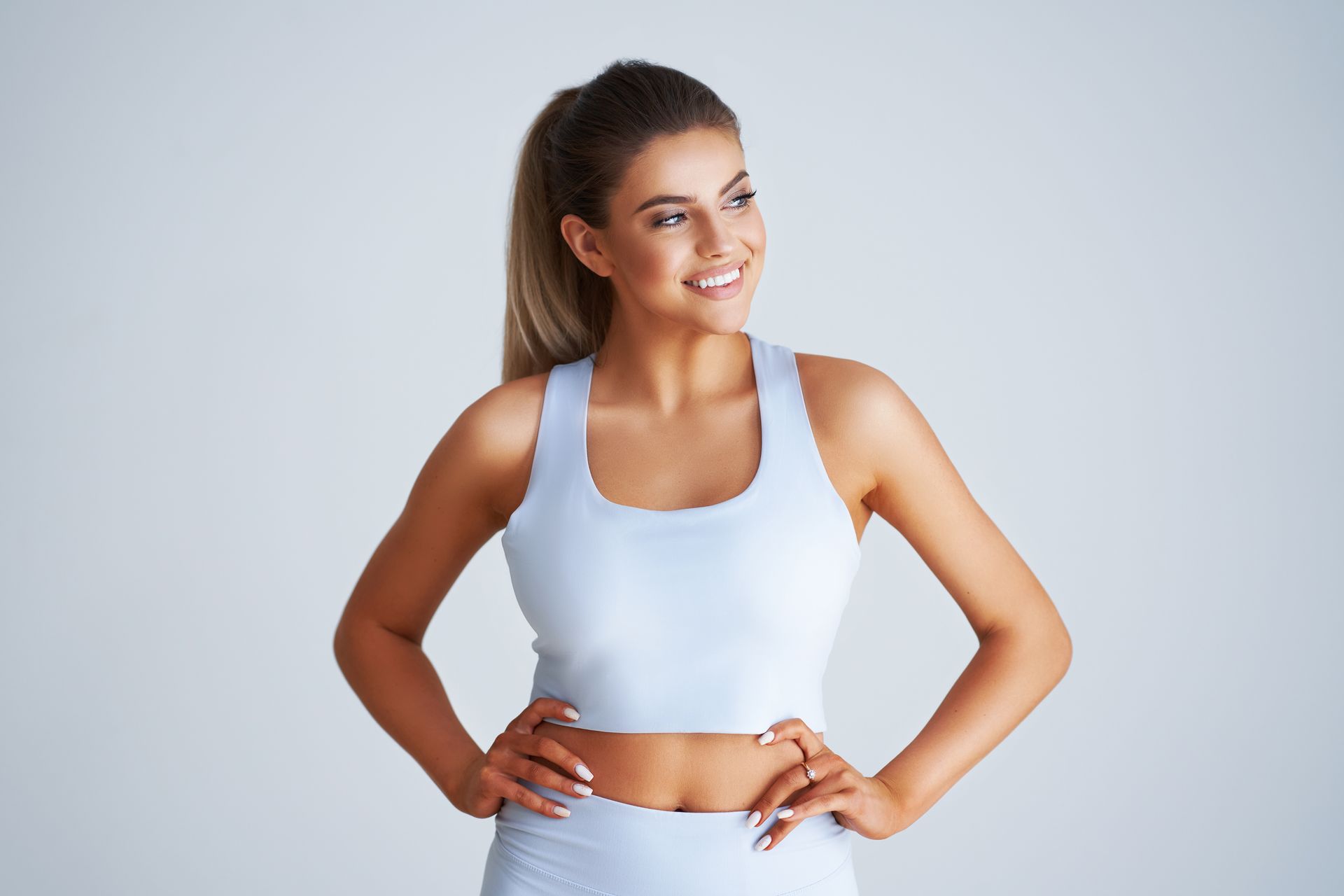 A woman is standing with her hands on her hips and smiling.