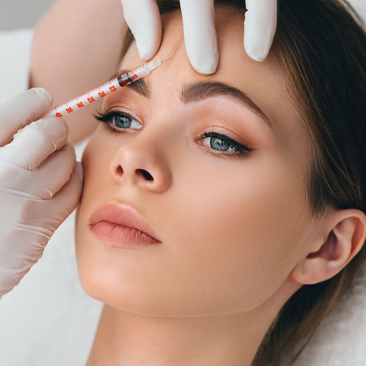A woman is getting a botox injection in her forehead.
