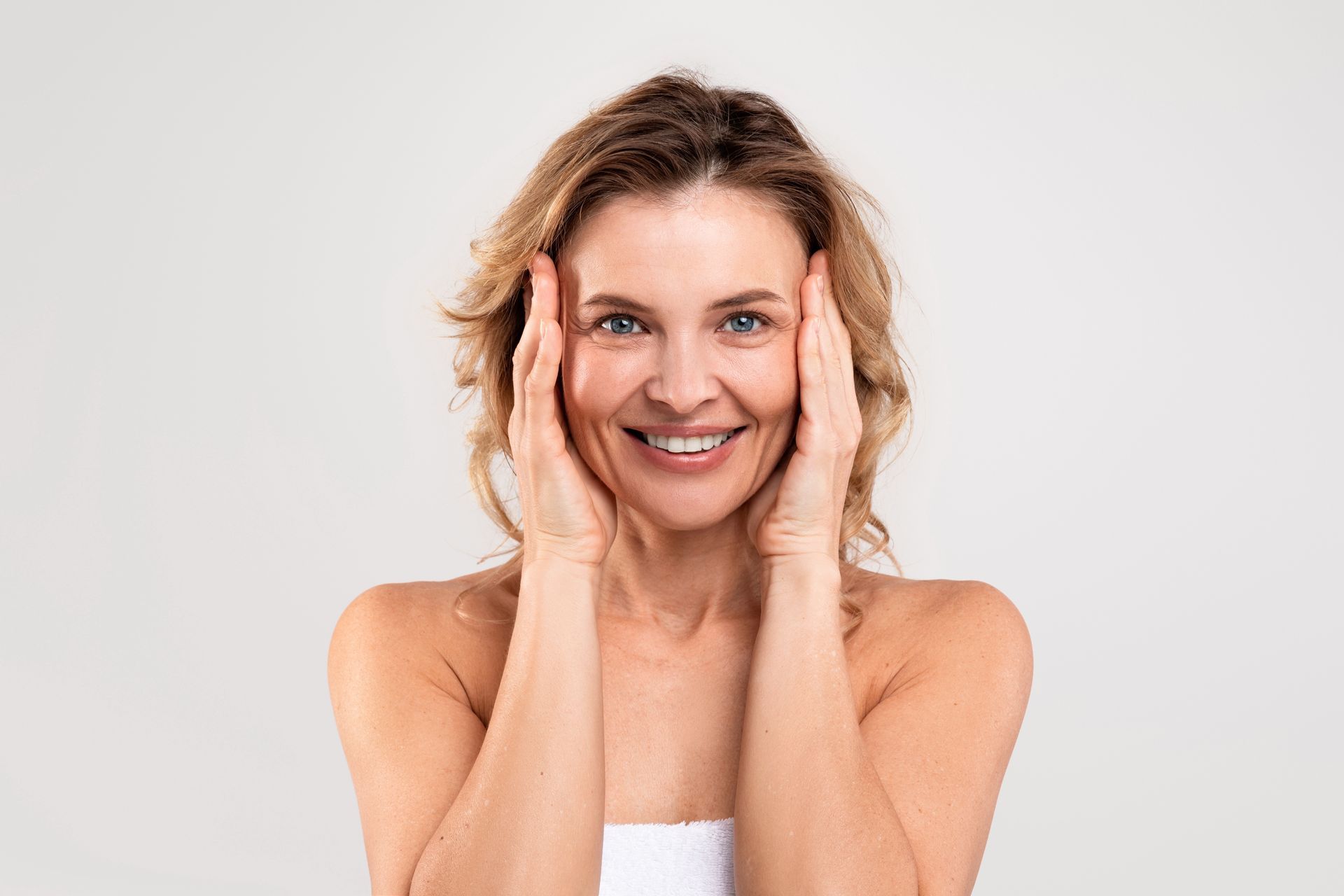 A woman is smiling and touching her face with her hands.