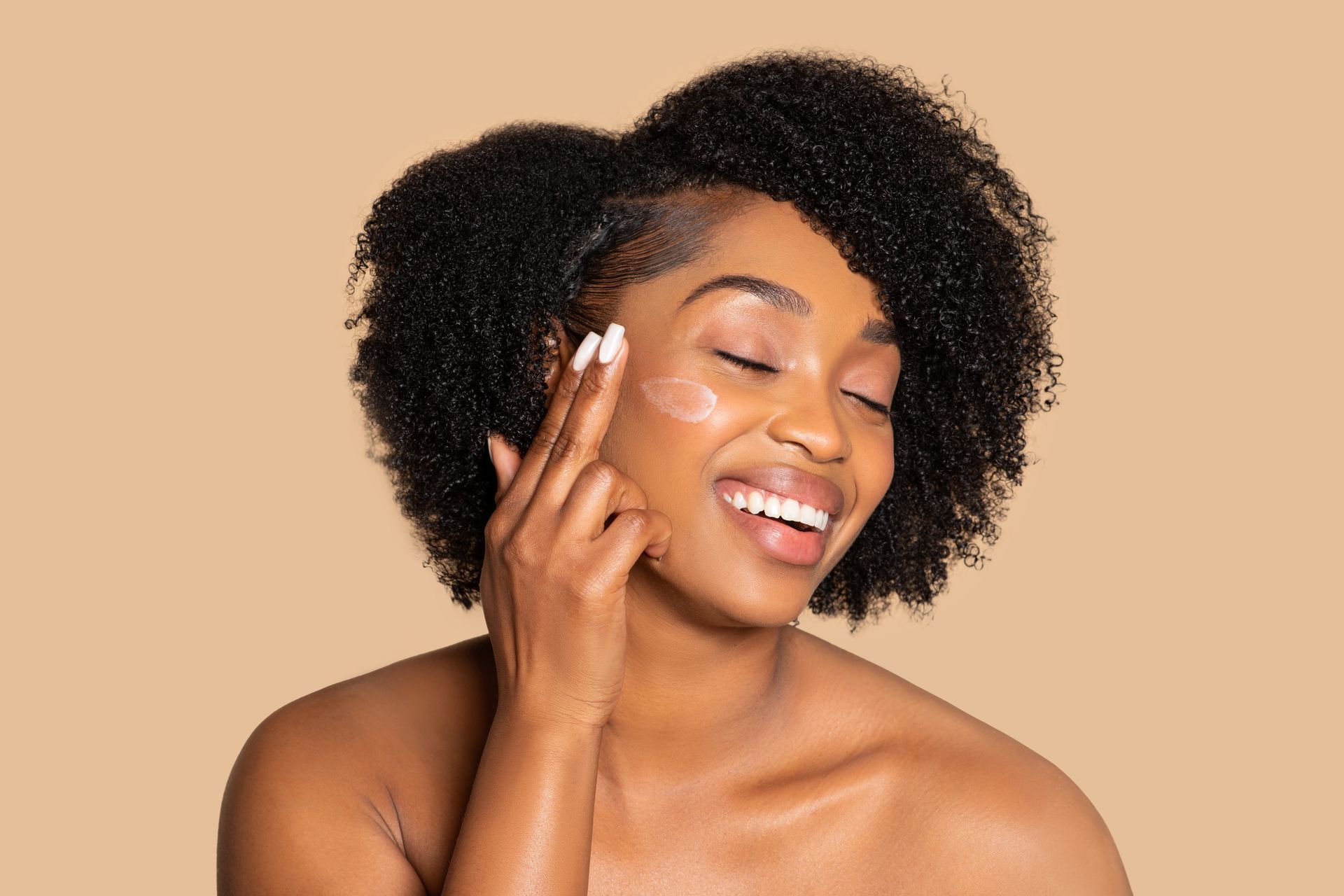 A woman is smiling while applying lotion to her face.