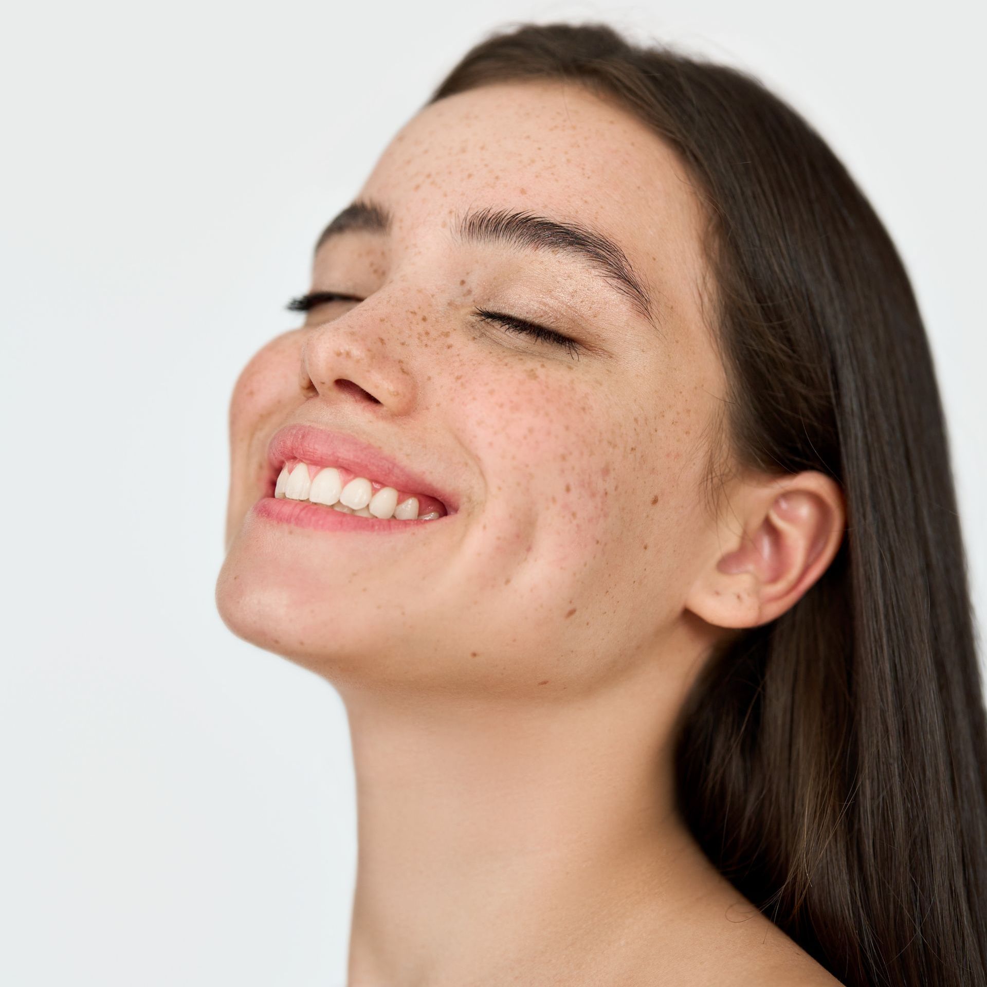 A woman with long hair and freckles is smiling with her eyes closed.