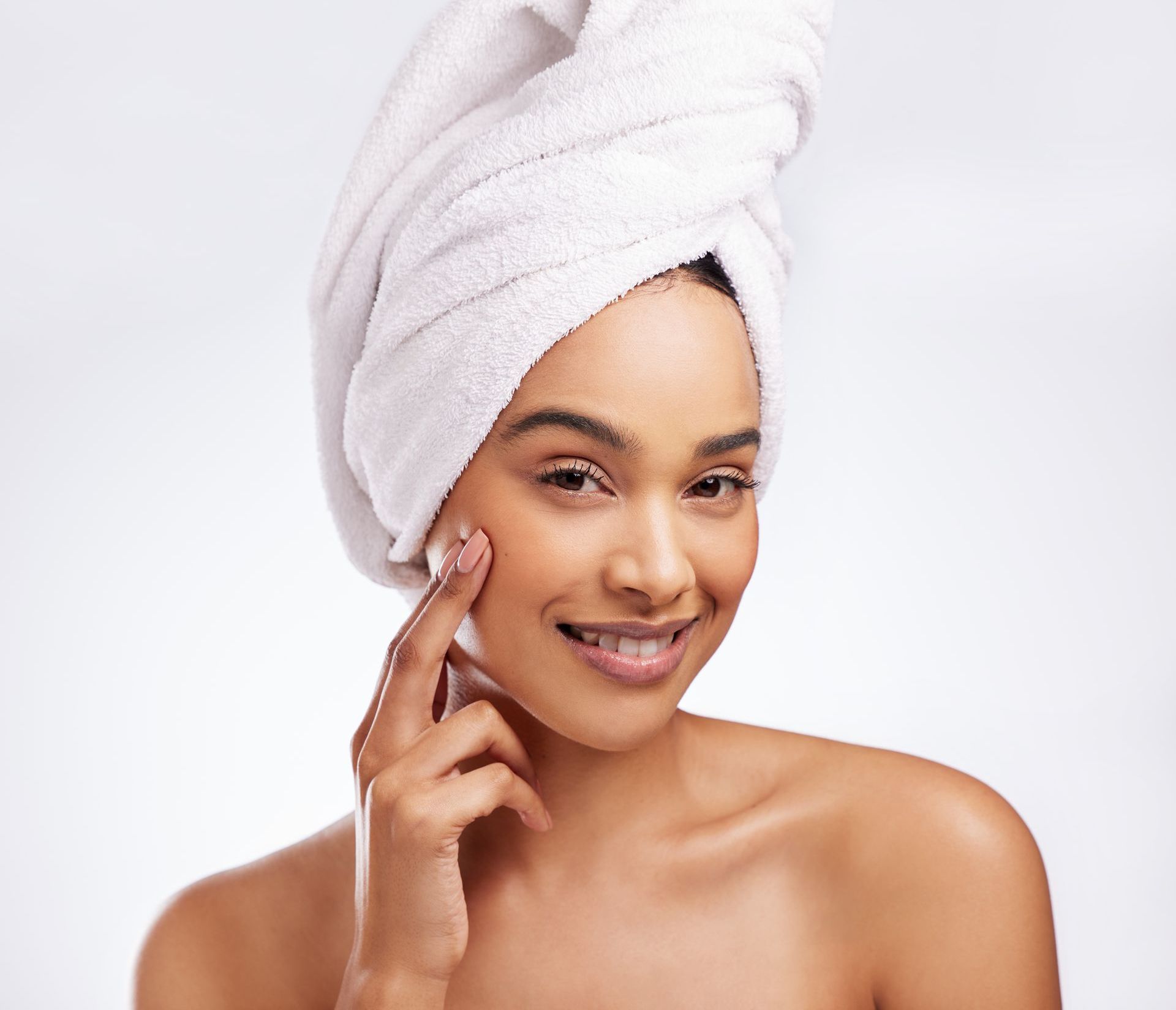 A woman with a towel wrapped around her head is smiling and touching her face.