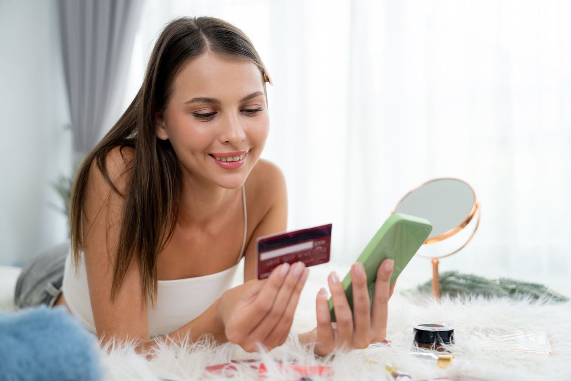 A woman is laying on a bed holding a credit card and a cell phone.