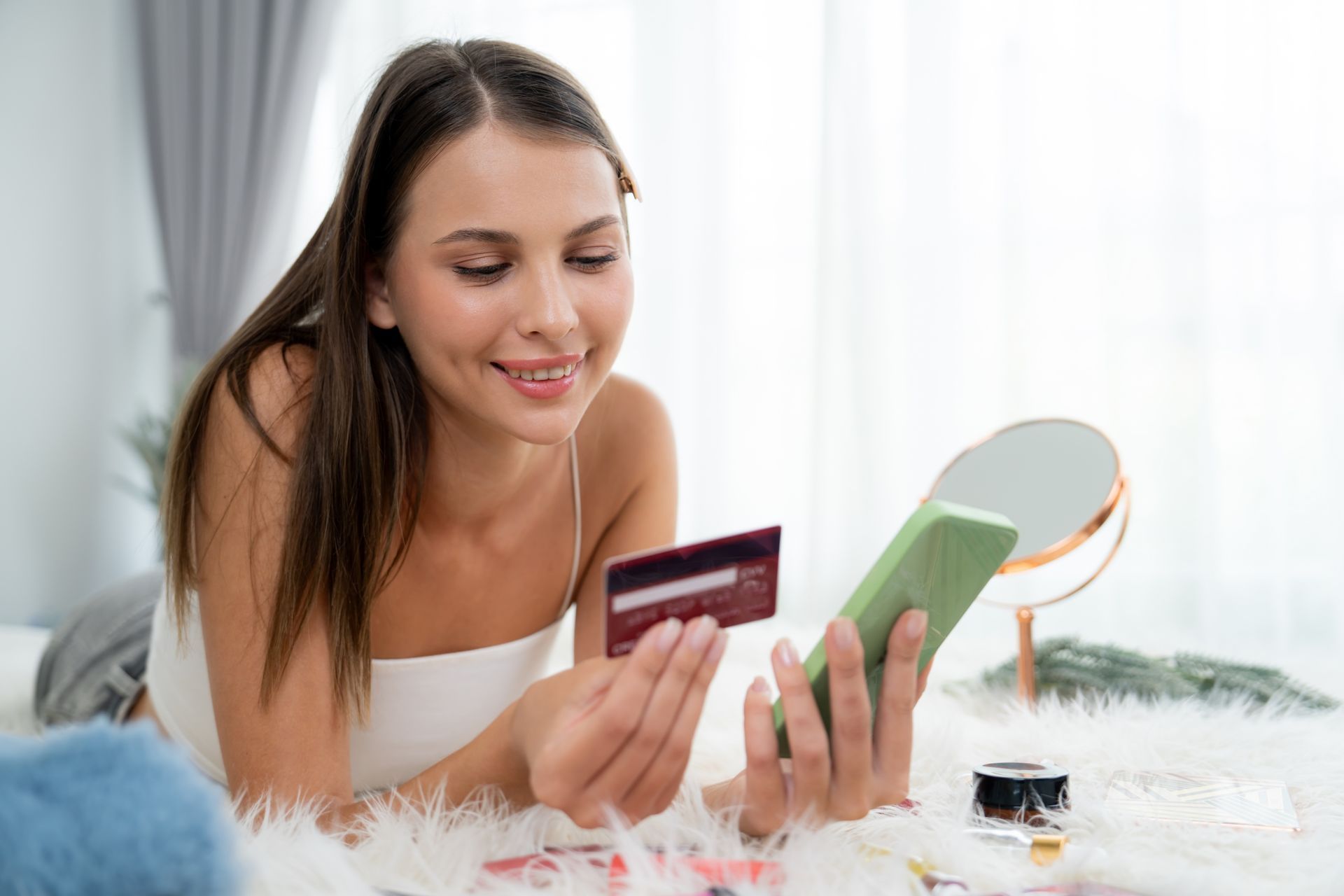 A woman is laying on the floor holding a credit card and a cell phone.