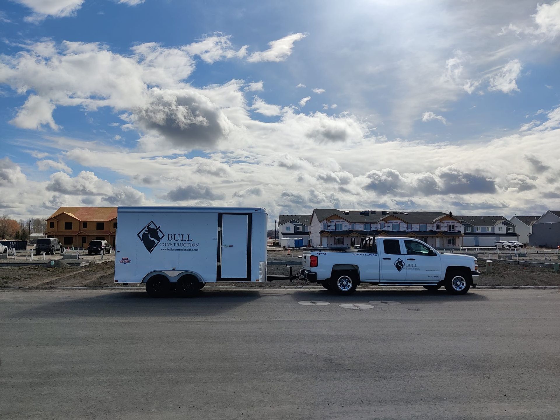 A white truck with a trailer attached to it is parked on the side of the road.