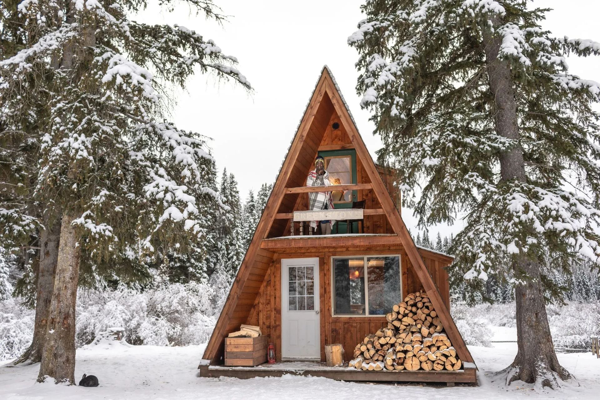 A small a frame cabin in the middle of a snowy forest.