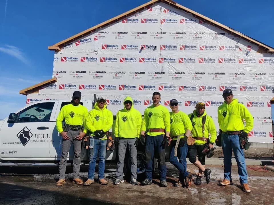 A group of construction workers are posing for a picture in front of a building under construction.