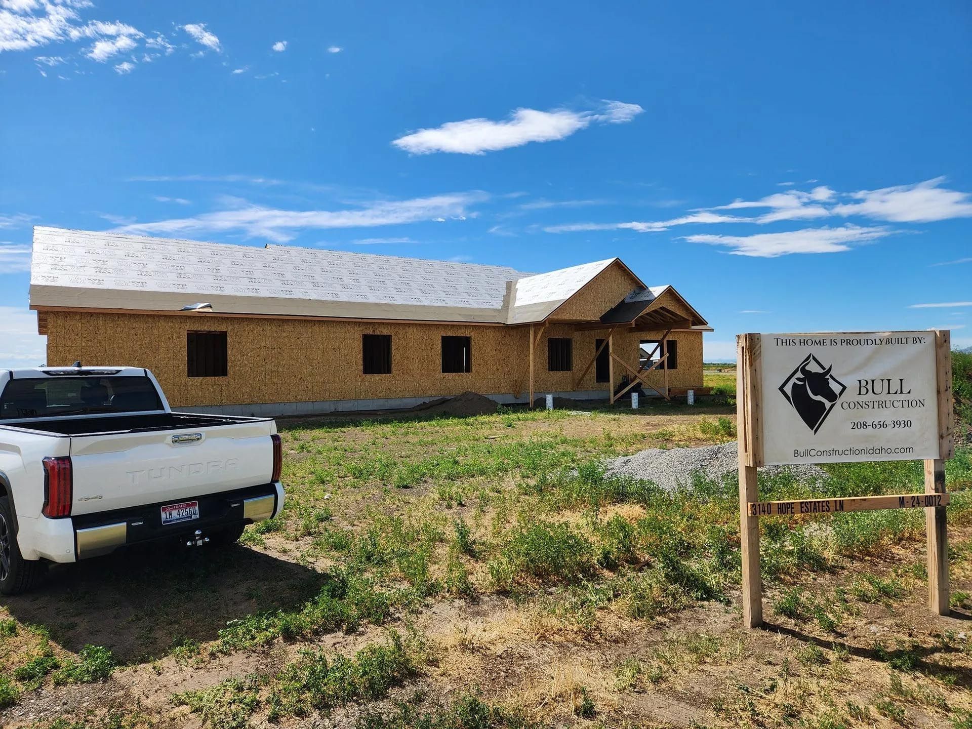 A white truck is parked in front of a house under construction.