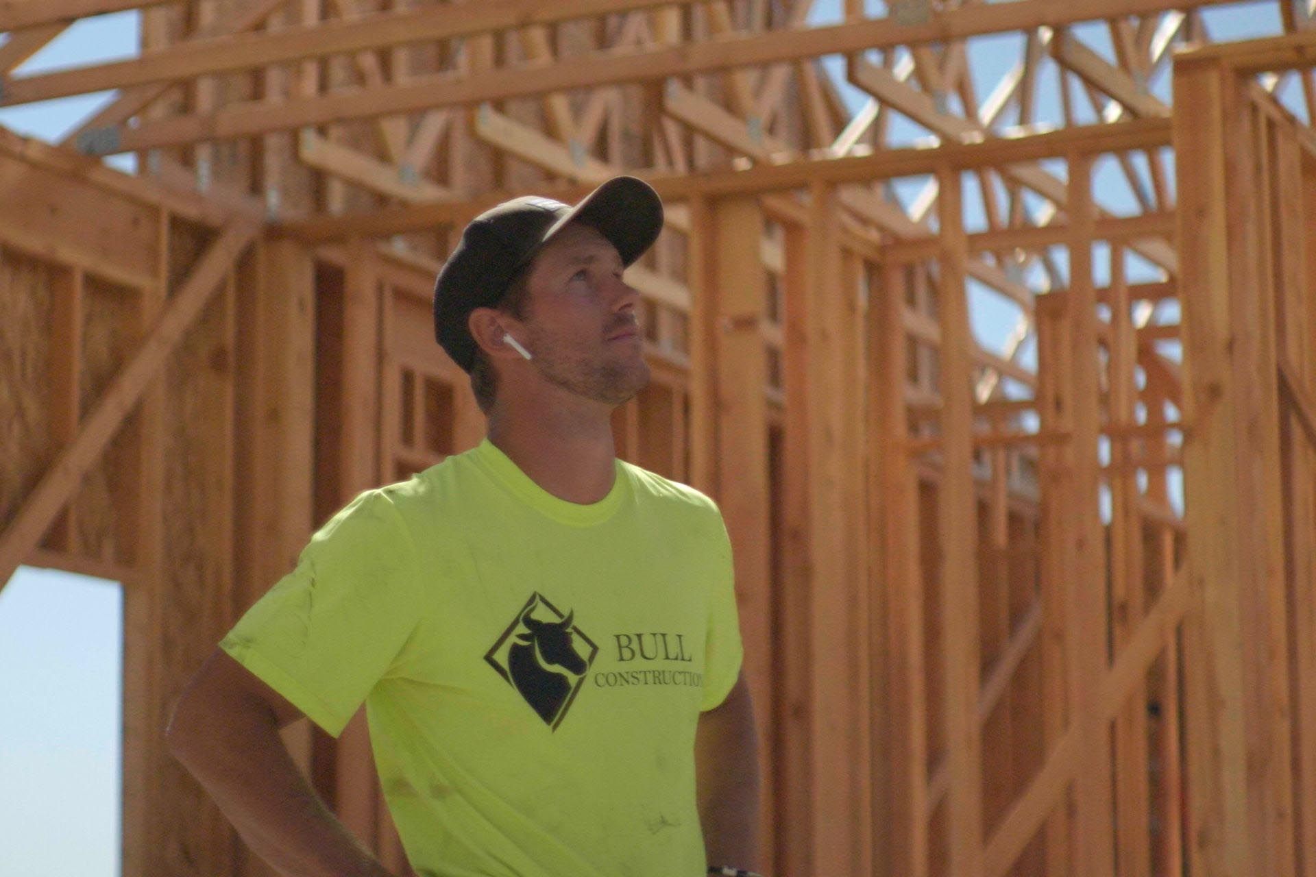 A man in a yellow shirt is standing in front of a wooden structure.